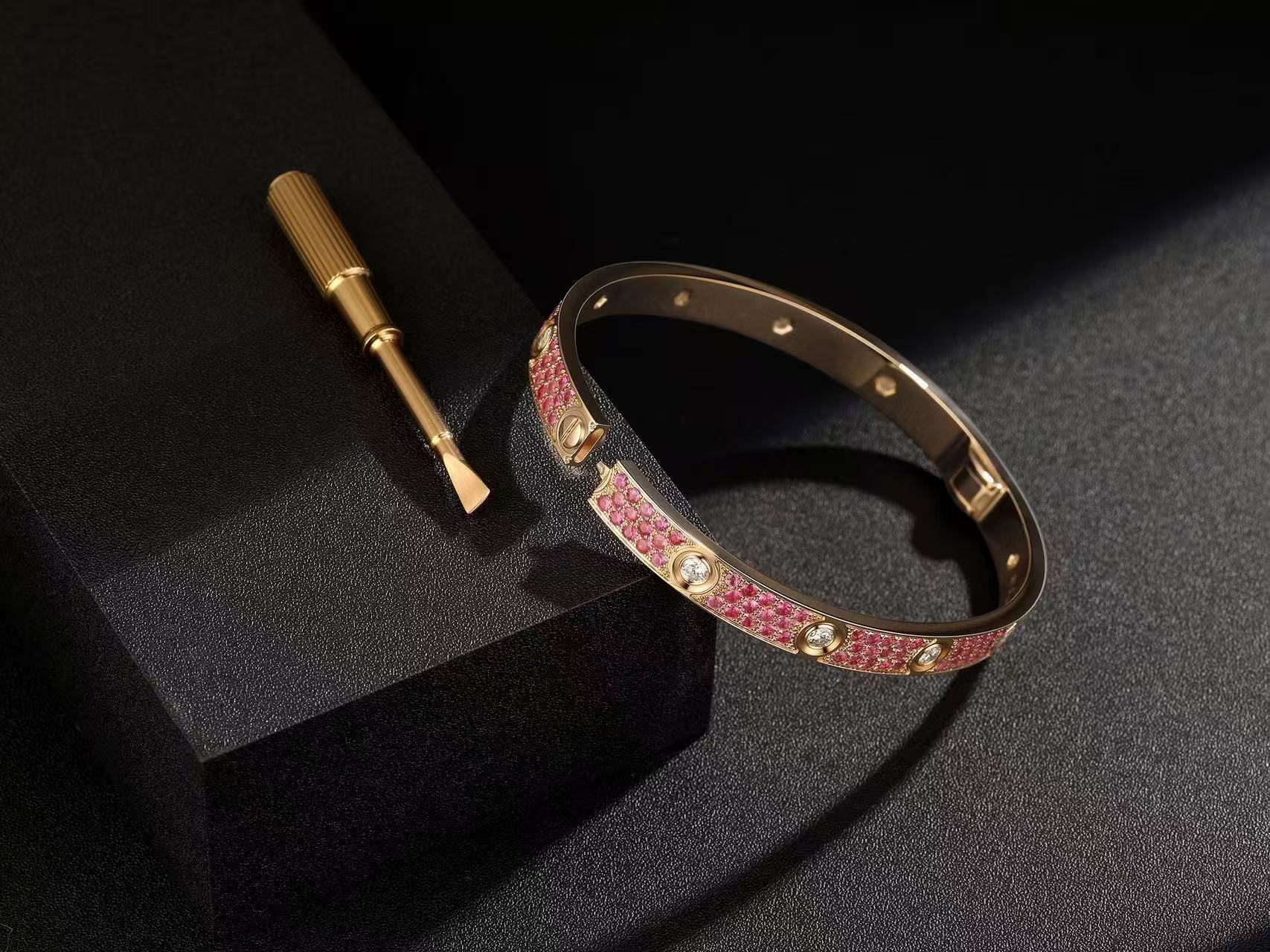 Pink pavé replica bangle shown open on a dark textured background beside a screwdriver