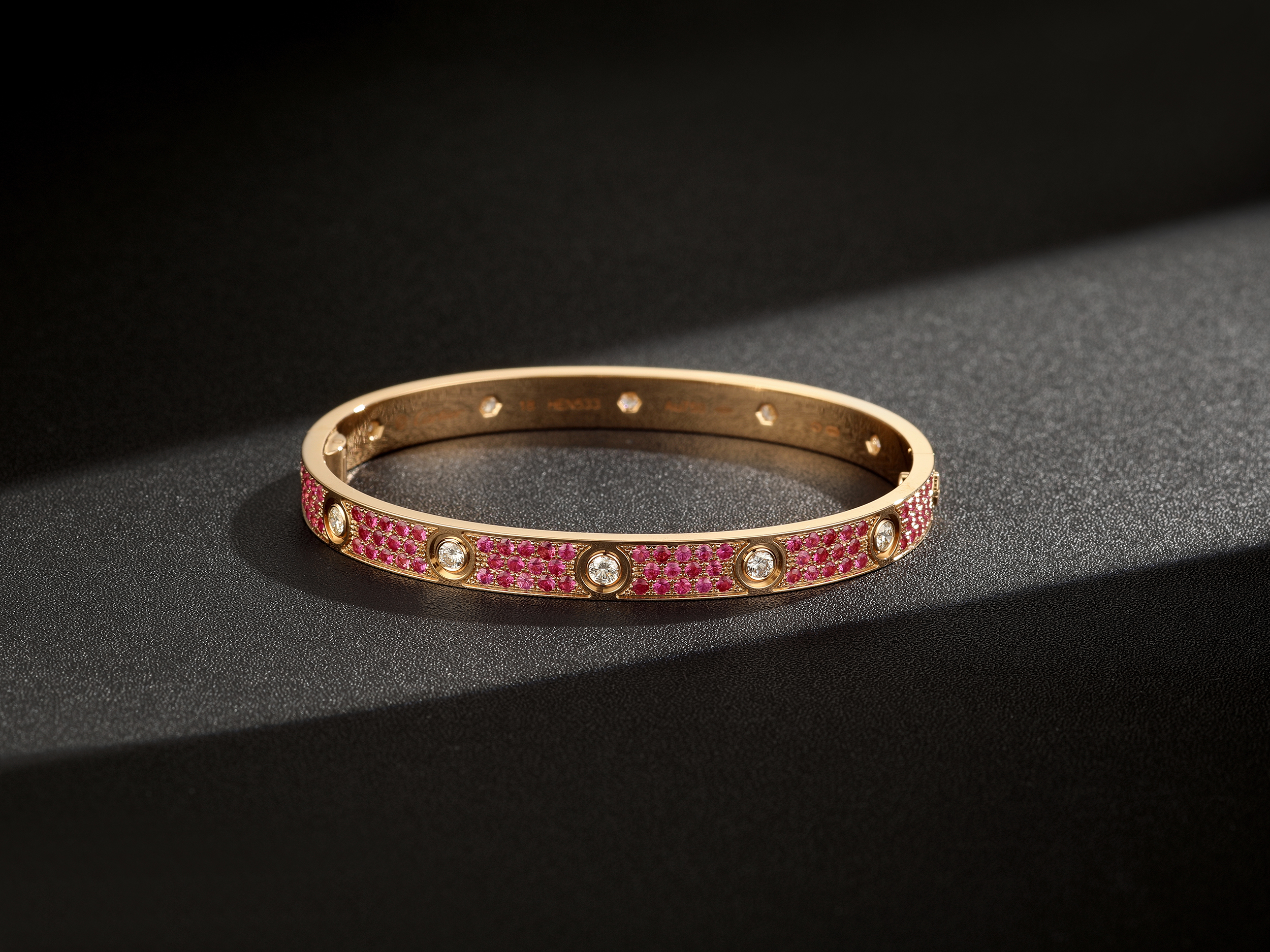 Pink pave replica bangle with round white stone accents on a dark textured background