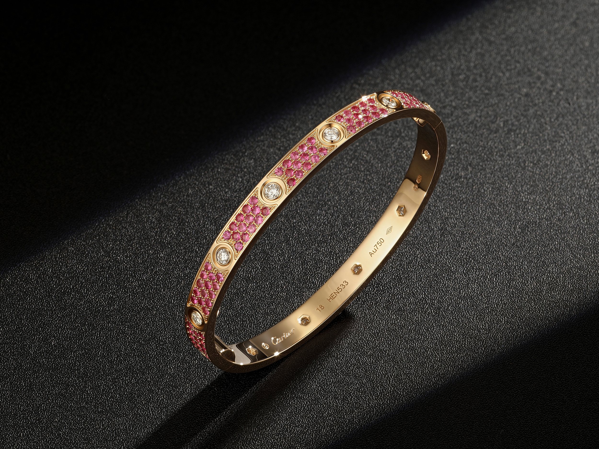 Angled view of a pink pavé LOVE style replica bracelet with larger round white stones and a polished inner band
